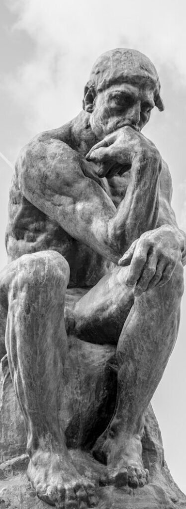 The thinker statue sits outdoors under a cloudy sky.